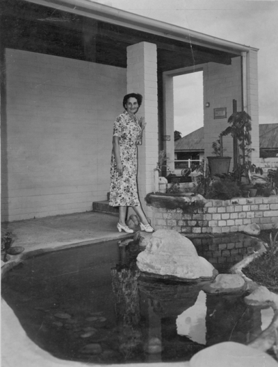 Gertrude Langer standing partially on a stepping stone in a garden pond.