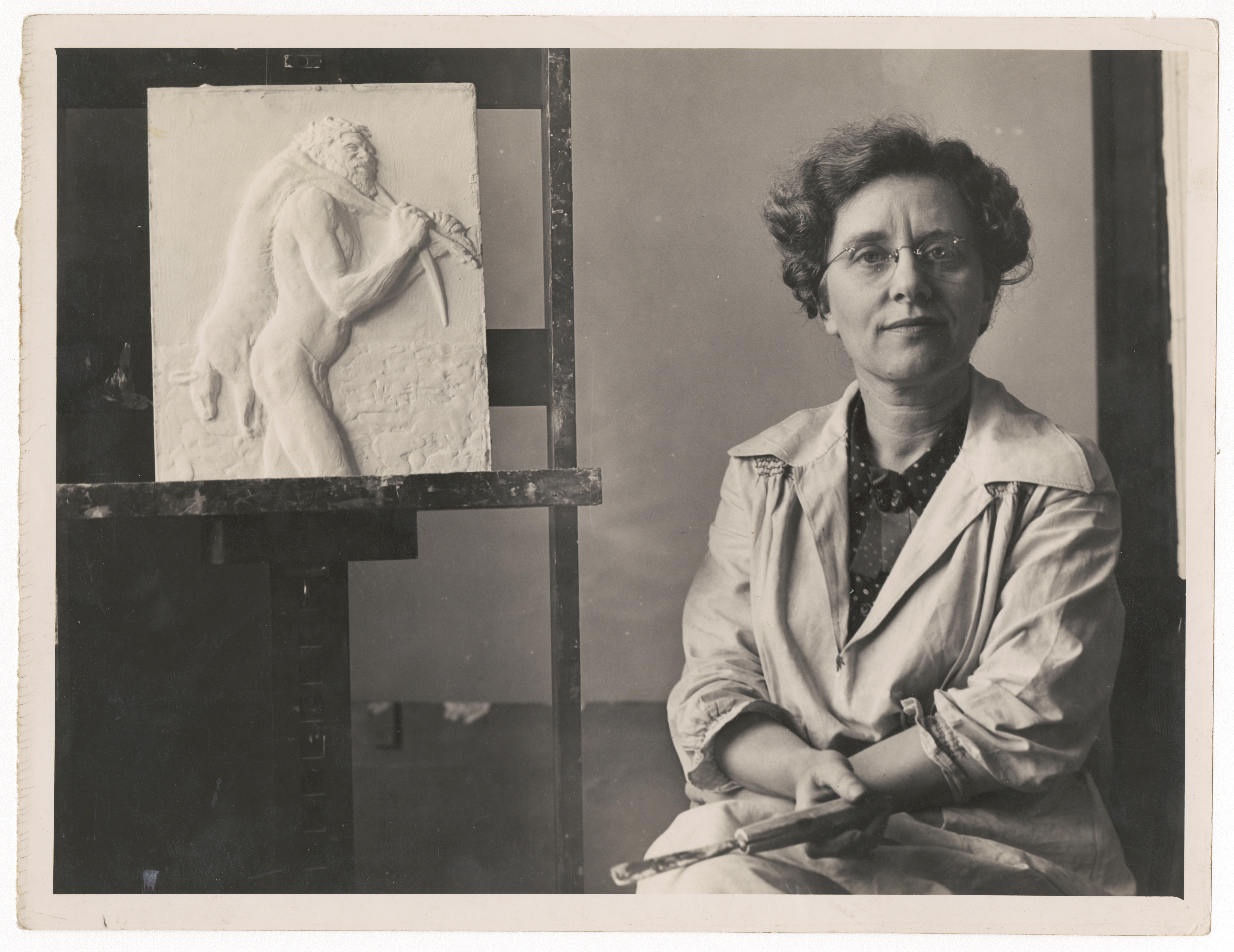 Daphne Mayo sitting in her studio, beside a panel for the east doors of the Public Library of New South Wales