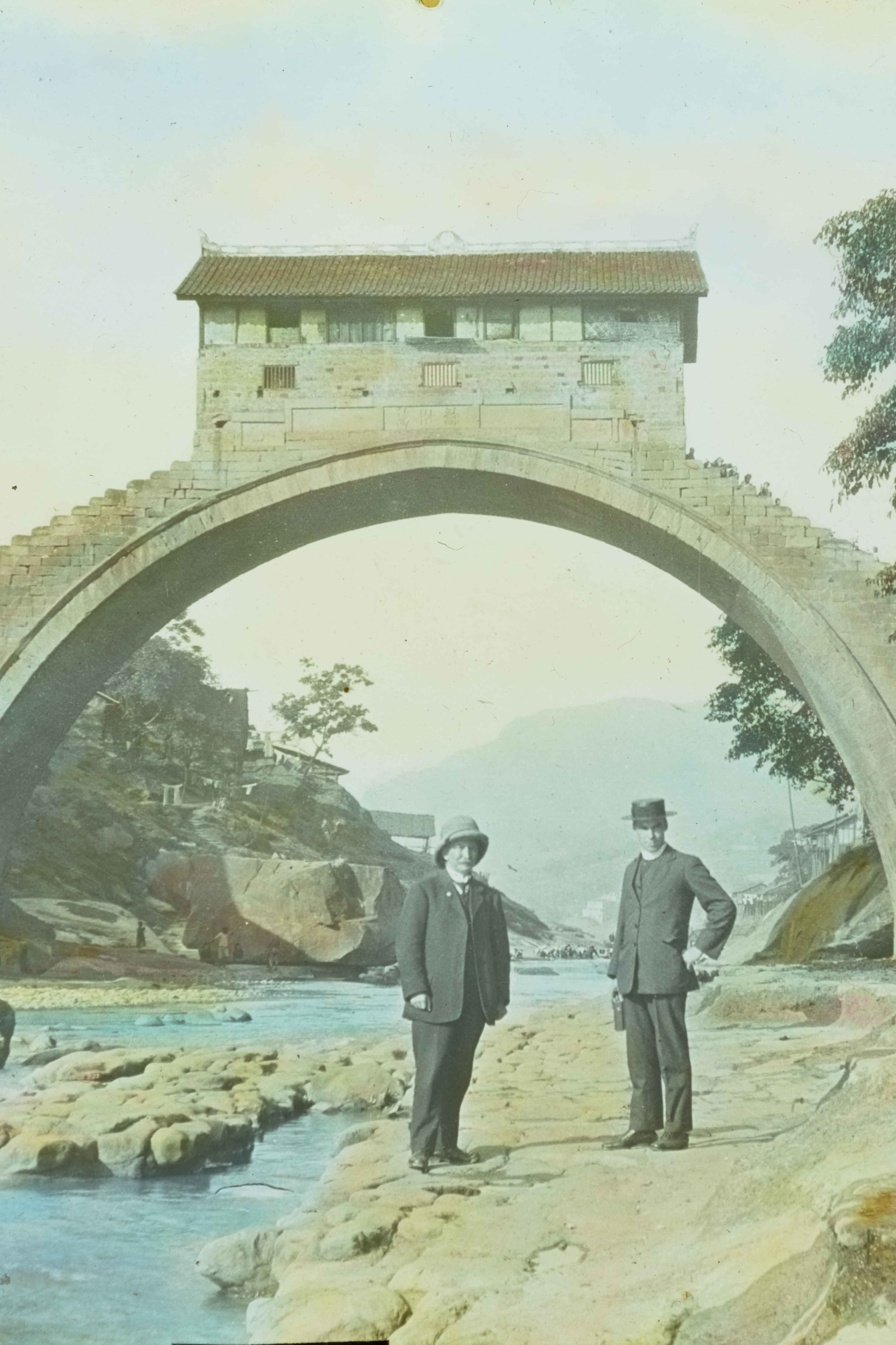 Two men standing in front of stone arch carring building bridge, possibly Asia