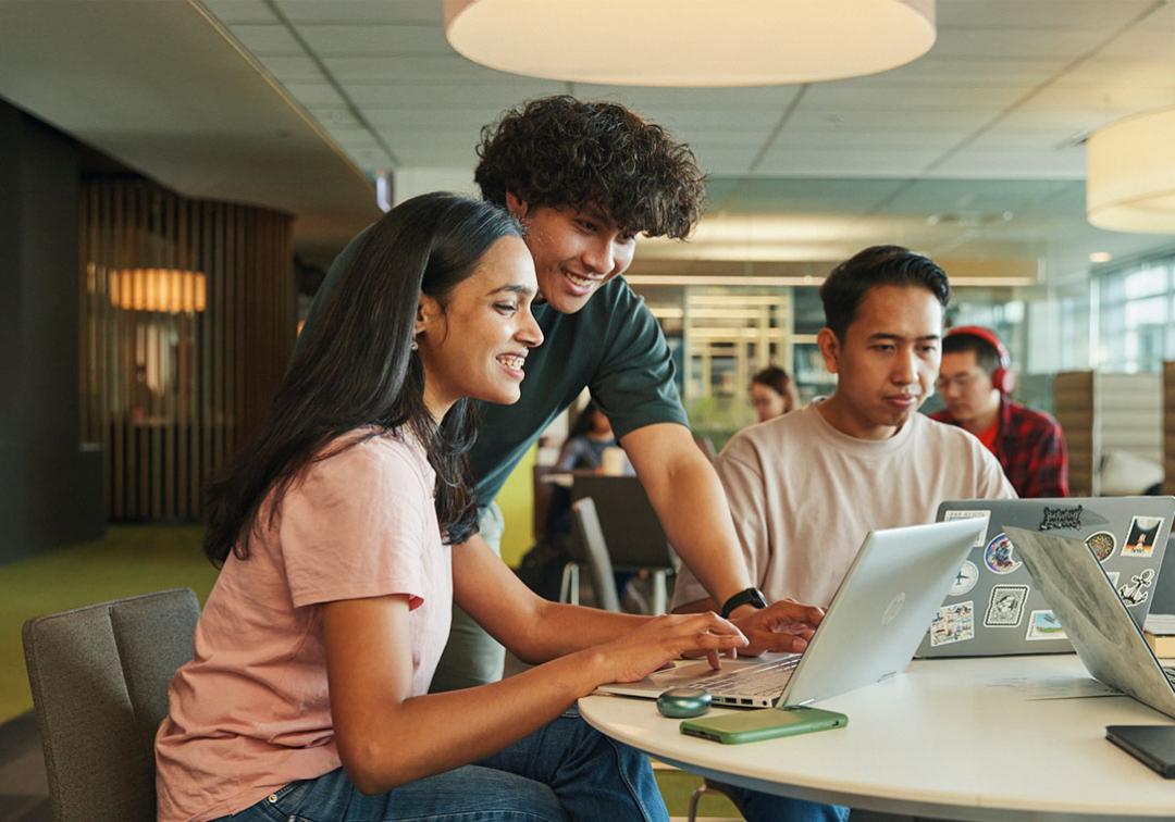 Three people at a desk looking and using laptops