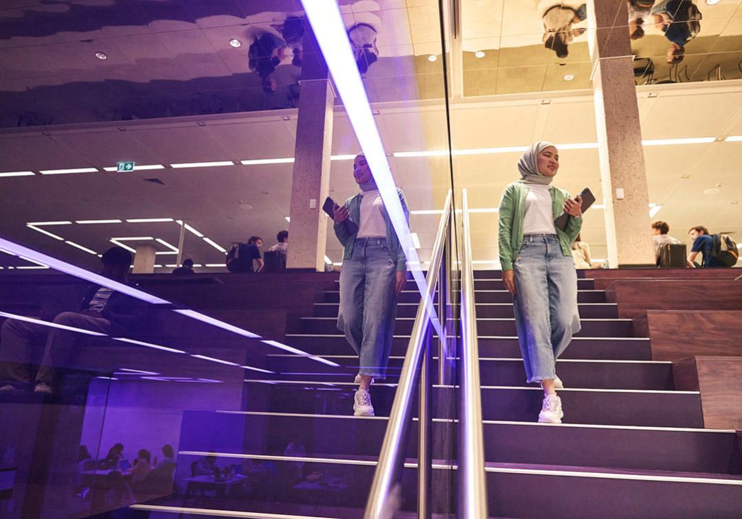 Student walking down the purple stairs in Central Library. She is reflected in the purple glass surrounding the stairs.