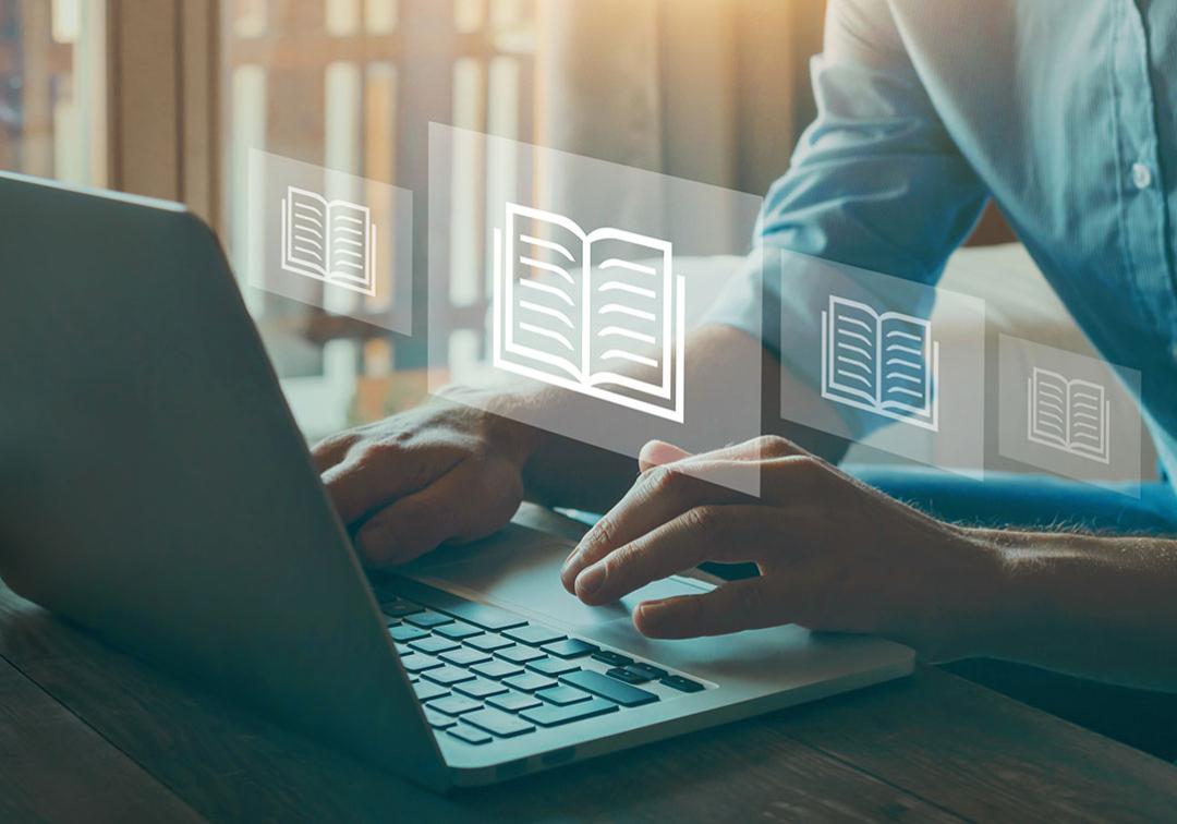 Person's hands at a laptop. Book symbols floating in the air.
