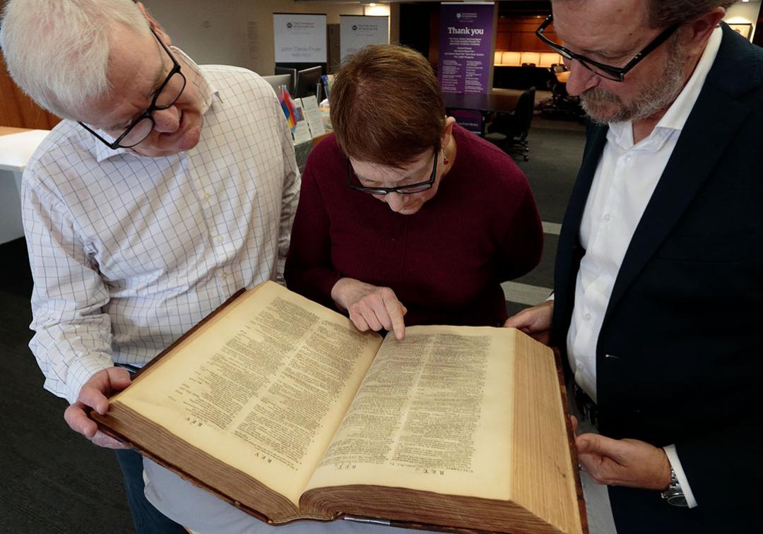 three people looking at a large open dictionary