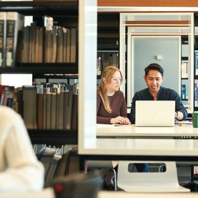 Students with a laptop, next to book shelves.