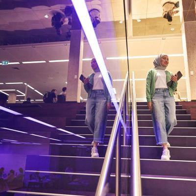 Student walking down the purple stairs in Central Library. She is reflected in the purple glass surrounding the stairs.