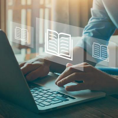 Person's hands at a laptop. Book symbols floating in the air.
