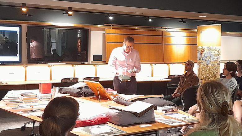 Librarian wearing white gloves showing a rare book to a class of Australian literature students in the Fryer Library teaching space.