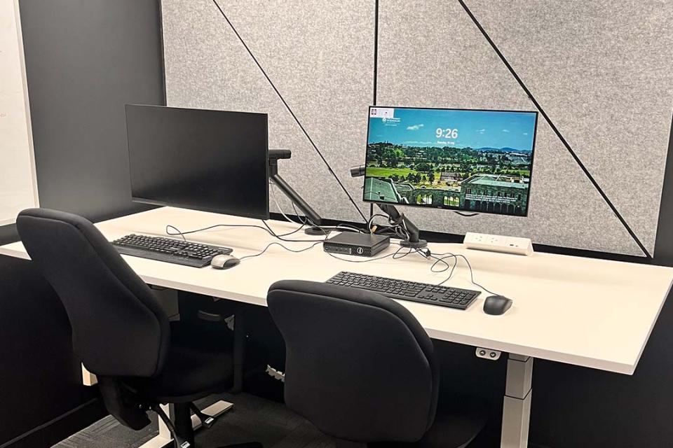 Assistive technology room setup with height-adjustable desk, computer screens, keyboards and mouses.