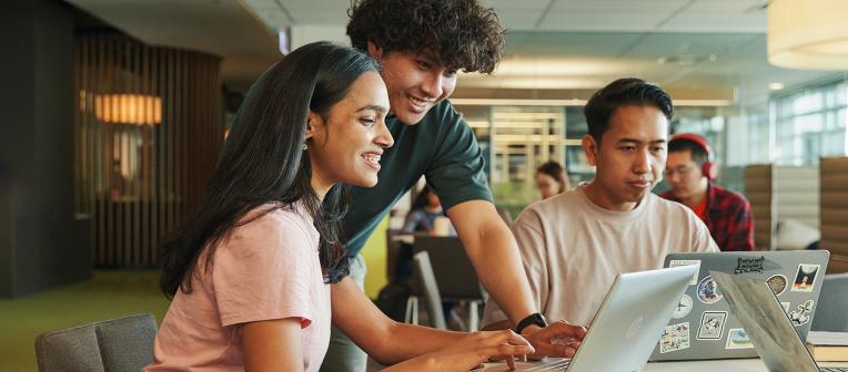 Three students looking at laptops at a desk