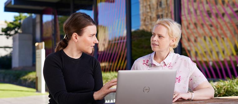 Staff talking outside at a table with a laptop in front of them.