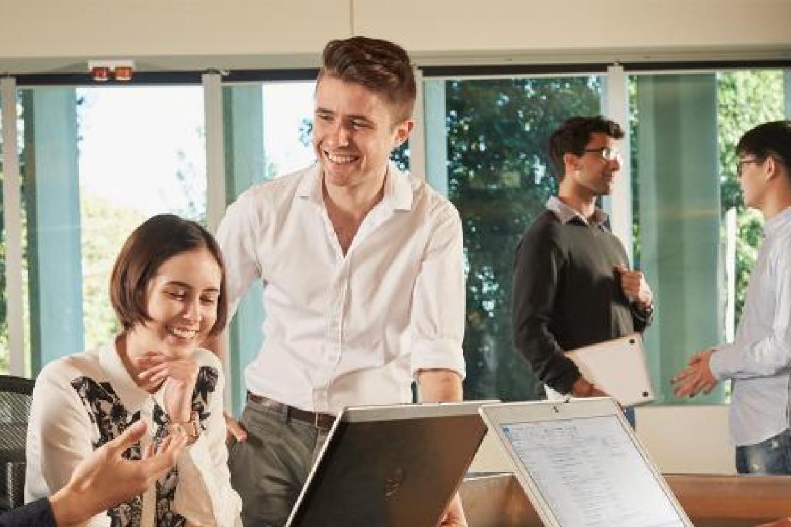 Teacher talking to students at a desk with open laptops