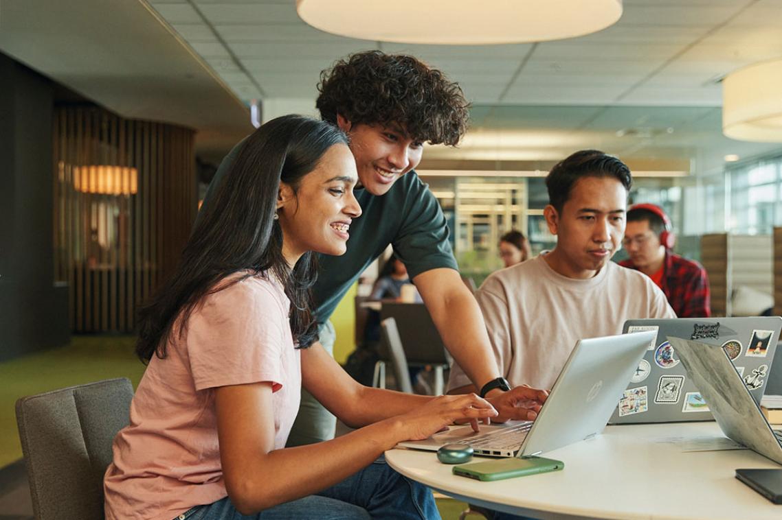 Three people at a desk looking and using laptops