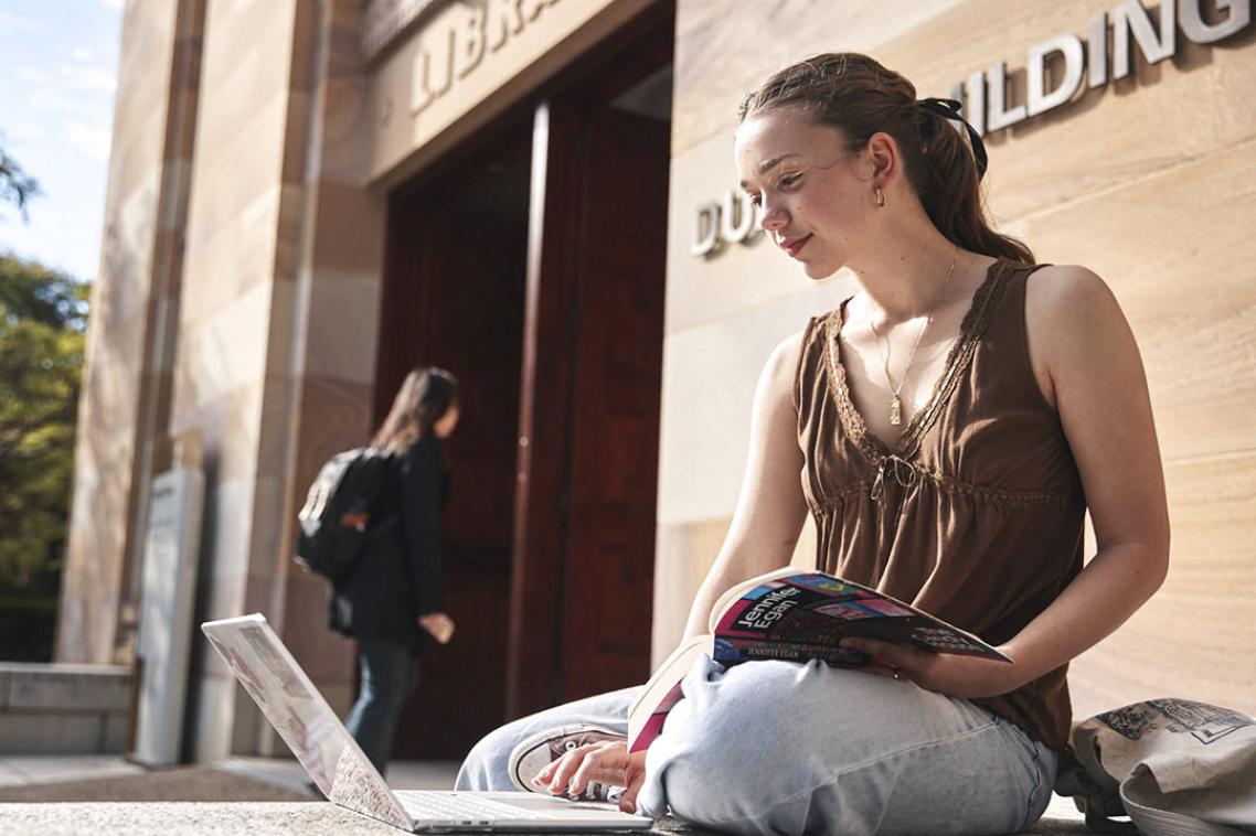 student with laptop outside library 