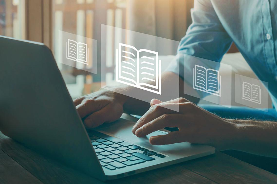 Person's hands at a laptop. Book symbols floating in the air.