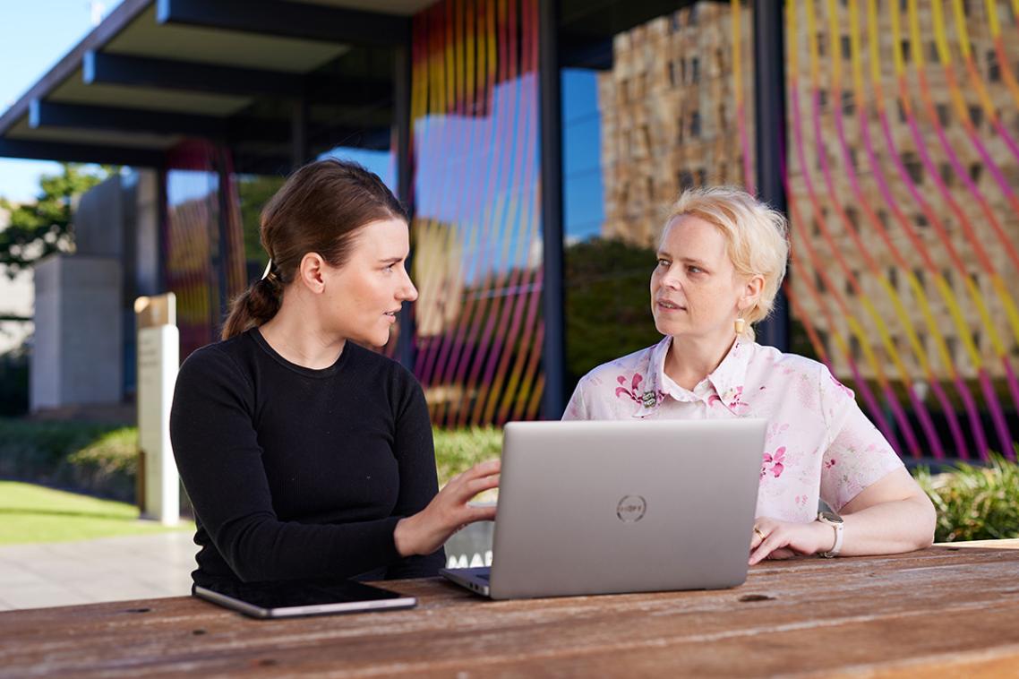 Staff talking outside at a table with a laptop in front of them.