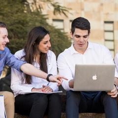 4 students sitting outside looking at a laptop screen